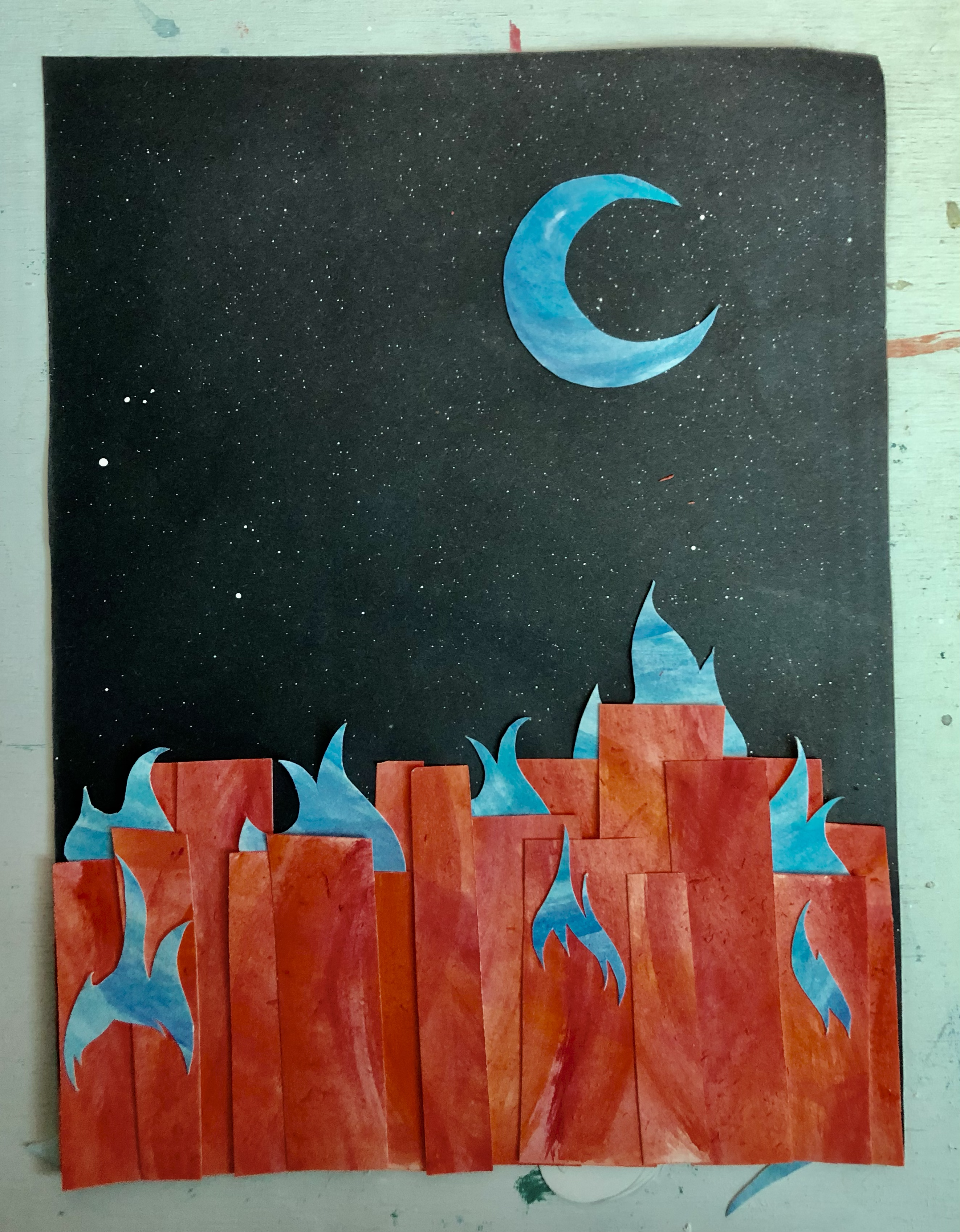 a paper collage on a black starry background with a red watercolor painting making buildings and a blue watercolor painting forming flames on the buildings and a moon in the sky